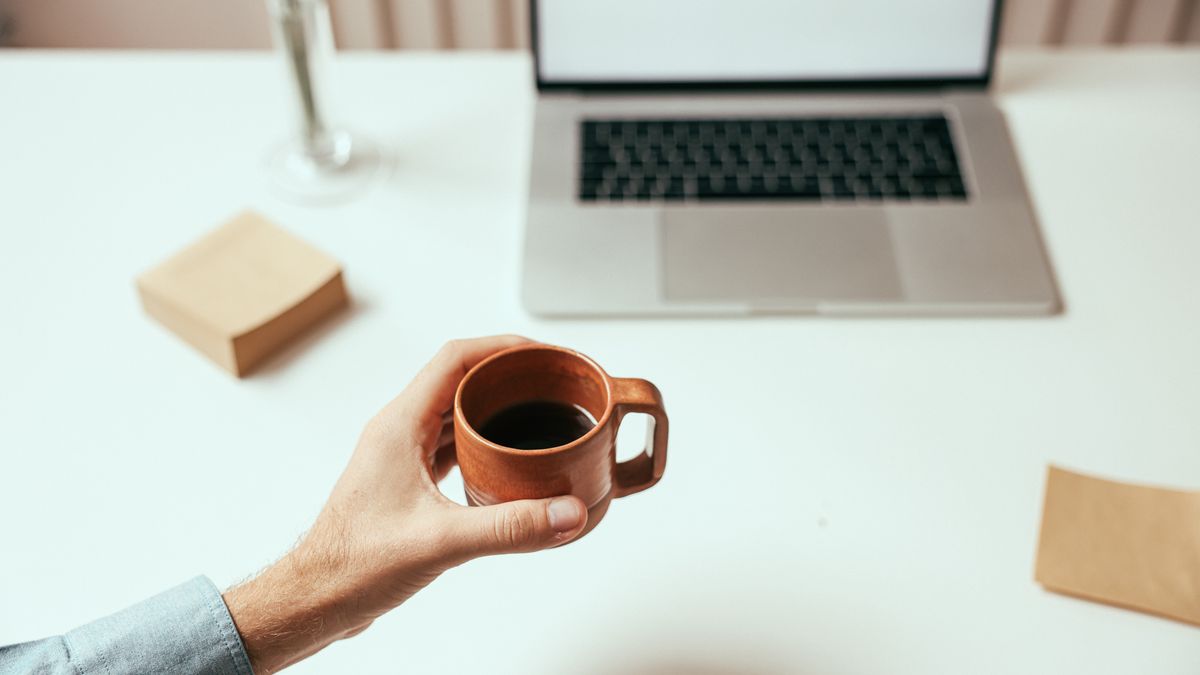A person holding a fresh coffee in an office with a coffee machine for the office in the background