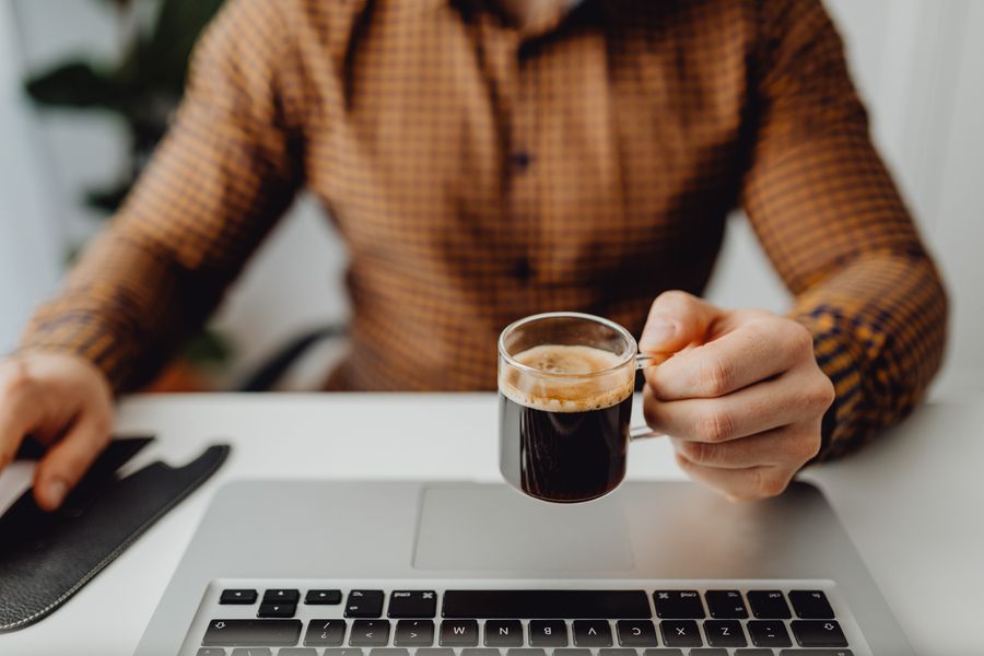 Office worker at a desk with a cup of coffee alongside a laptop in a modern workplace