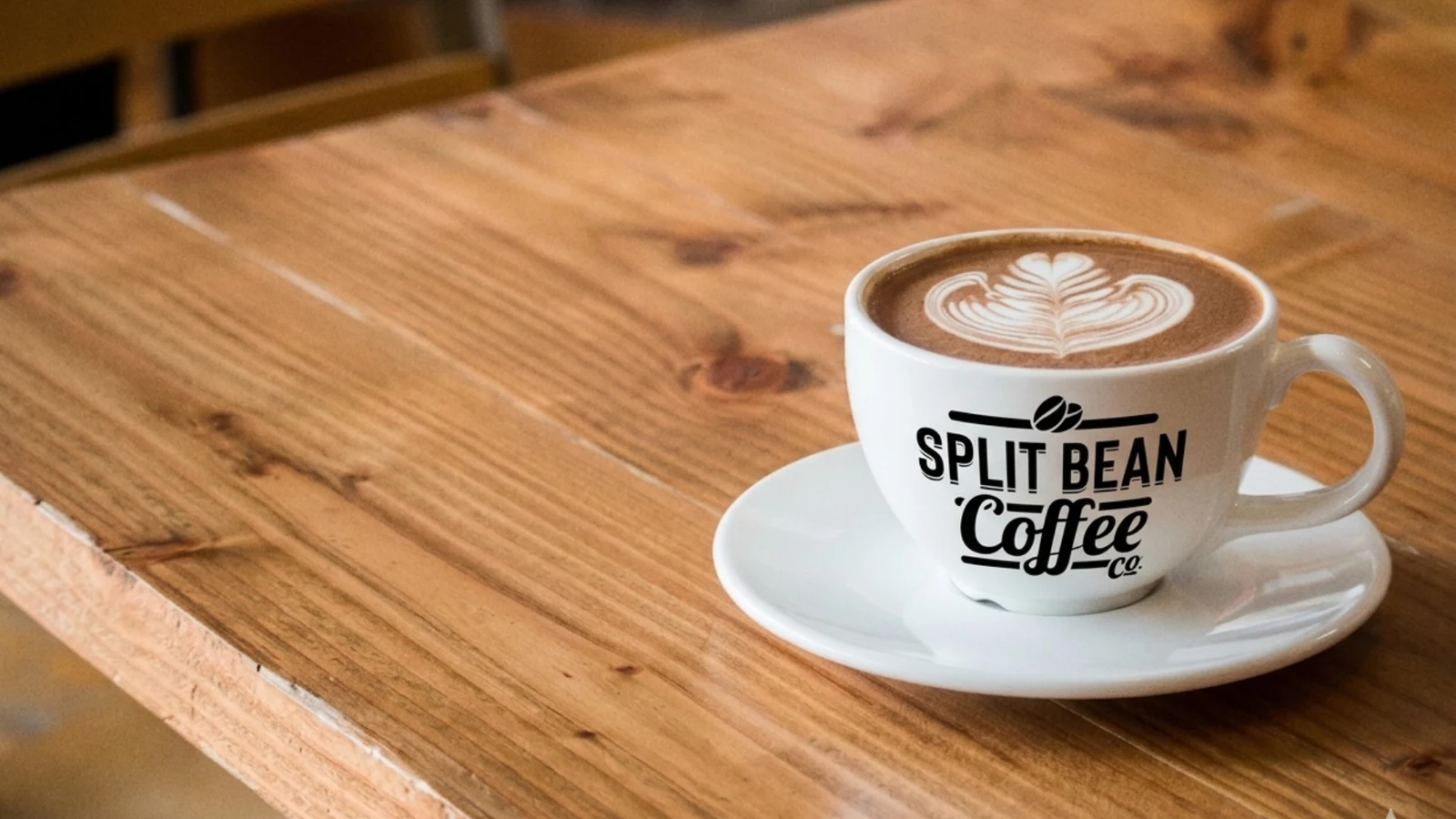 Cappuccino with latte art in a Split Bean Coffee branded cup on a wooden cafe table