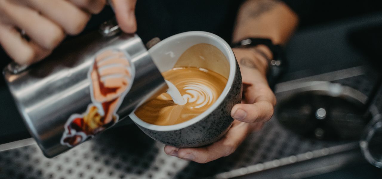 A barista pouring latte art into a cup of coffee